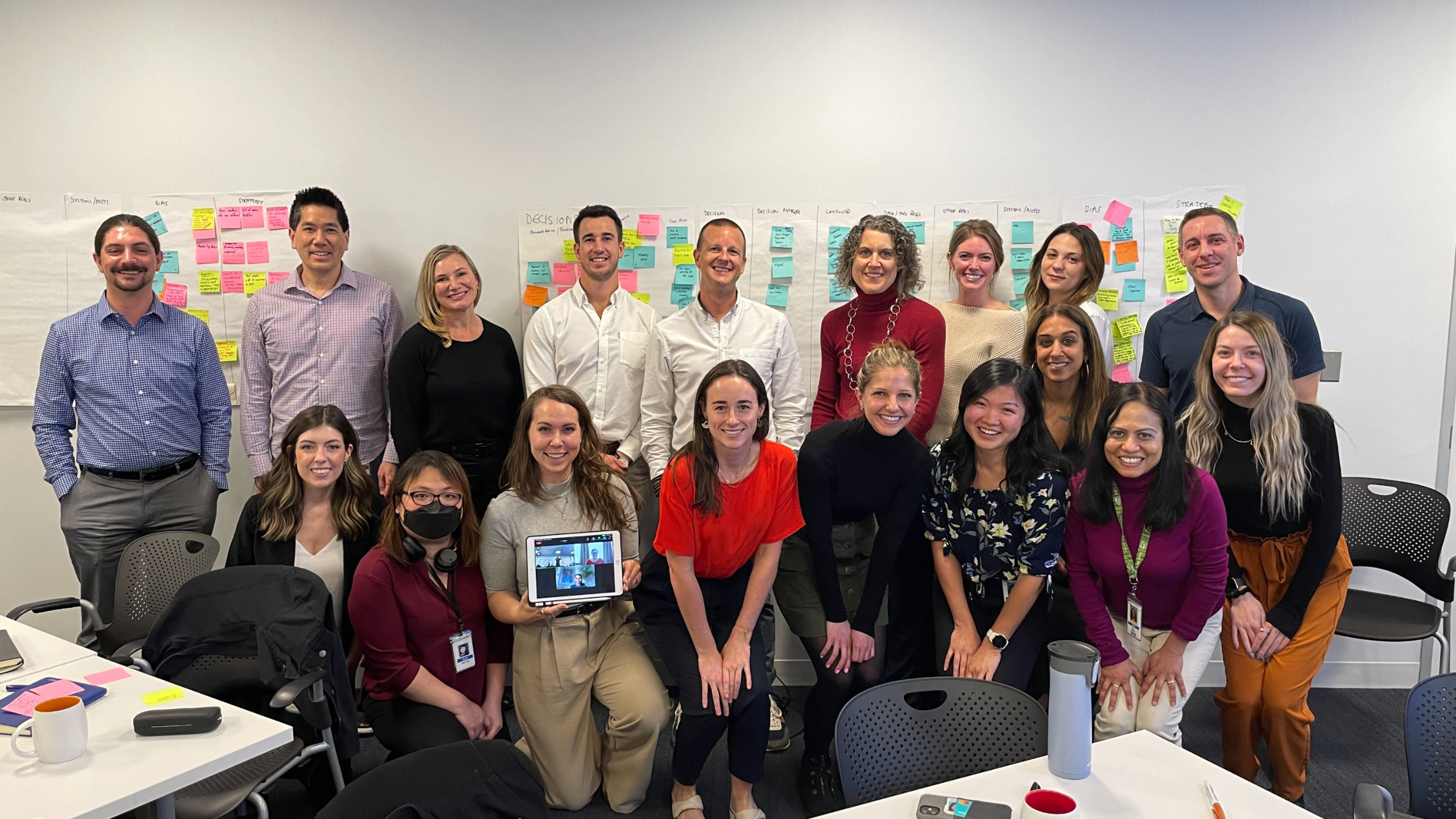 Smiling team group photo during leadership workshop with colorful sticky notes on wall.