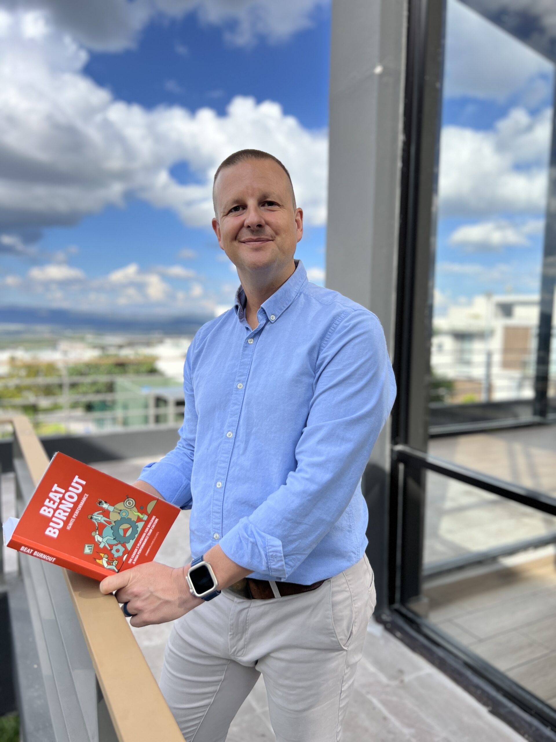 Jimmy Burroughes holding his book Beat Burnout on a sunny balcony.